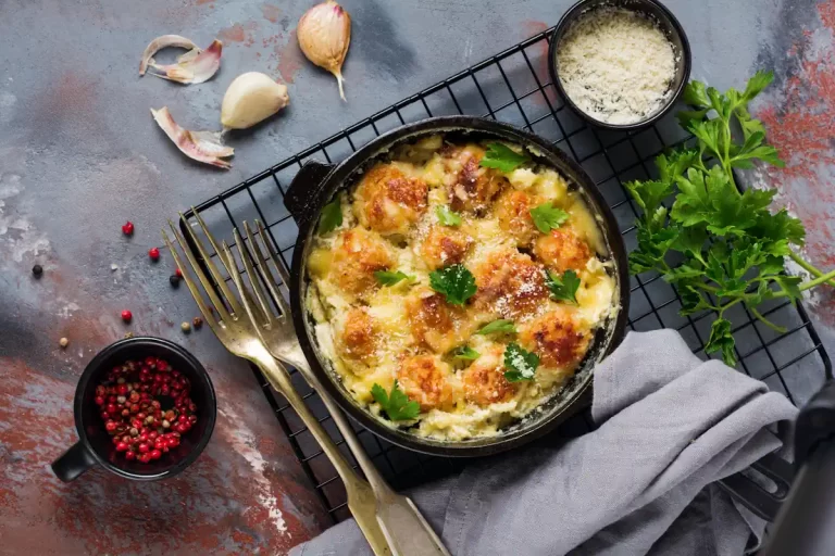 Un plat de gratin de fruits de mer servi sur plateau en forme de grillage à côté de bol de sauce de gousses d'ail