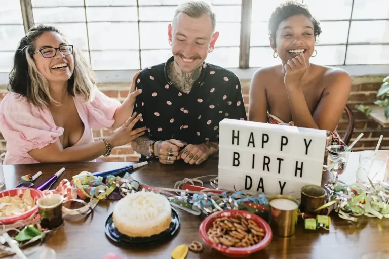 Un homme et deux femmes devant une table plein de plats et avec le mot Happy birthday