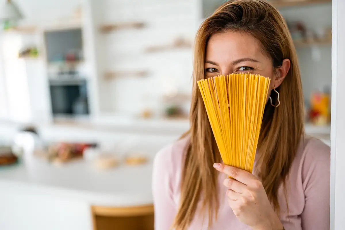 Une femme qui tient des pâtes en cachant sa bouche